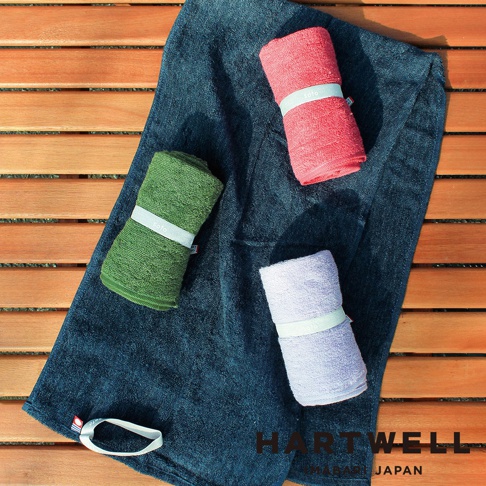 三條捲起來的戶外乾爽毛巾，分別是粉紅色、綠色和淺紫色，放在深藍色毛巾上，背景是木紋桌面。