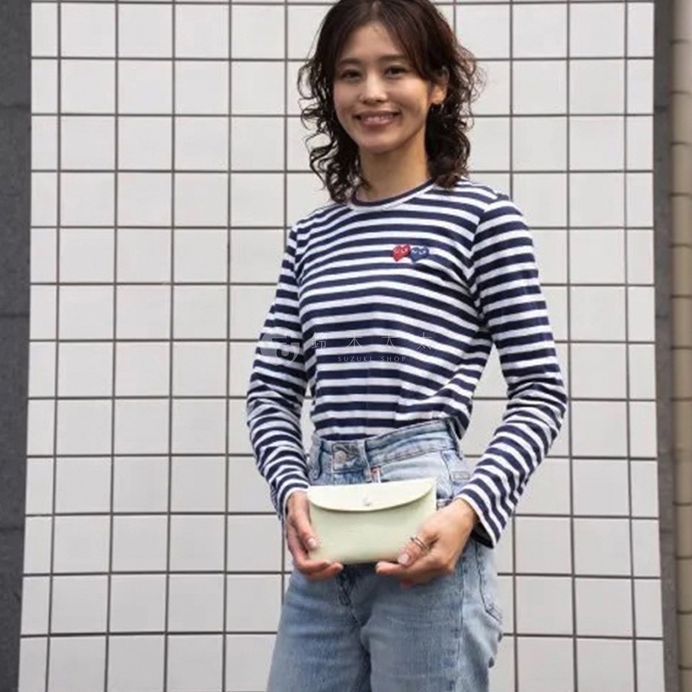 一位女性手持淺綠色、翻蓋式、皮革材質的京都職人手作多功能收納包，包上有一顆銀色鈕扣。