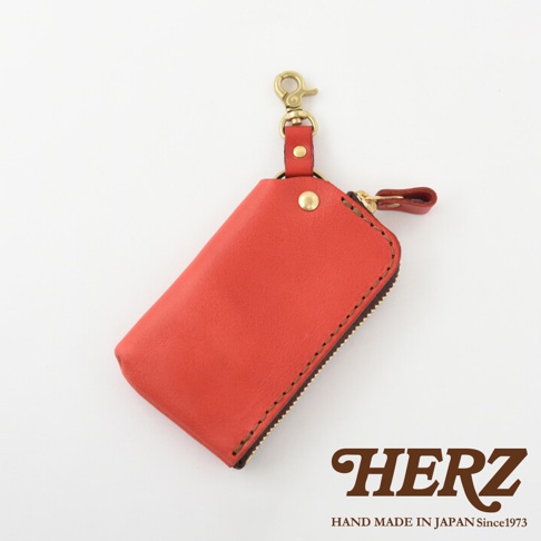 紅色皮革鑰匙包，設有金色掛鉤、拉鍊及皮革拉環，邊緣以深色線縫製。