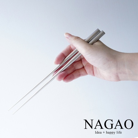 一雙銀色不鏽鋼筷子，由手部握持，筷子末端為尖形，整體呈現簡約的設計風格。