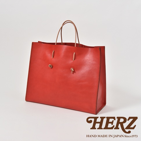 紅色皮革提袋，設有兩條皮革提把，正面有兩個皮革繫帶裝飾。