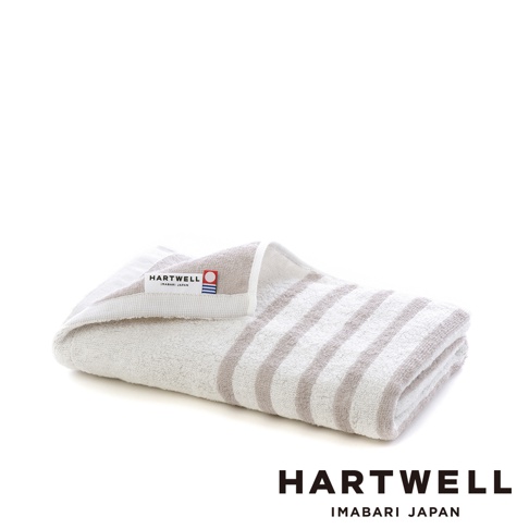一條折疊的迷你浴巾，淺灰色與米白色條紋，毛圈材質，左側有 HARTWELL IMABARI JAPAN 品牌標籤。