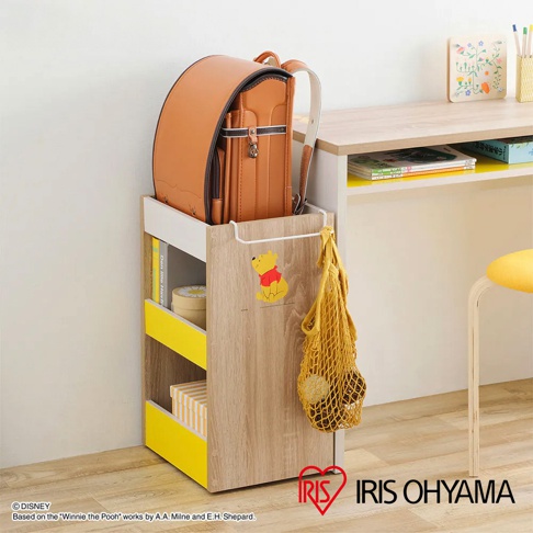 迪士尼系列木質收納櫃，附滾輪，淺木紋外觀，搭配黃色點綴。櫃體上方放置棕色日式書包，側邊有小熊維尼圖案，並掛有黃色網袋。