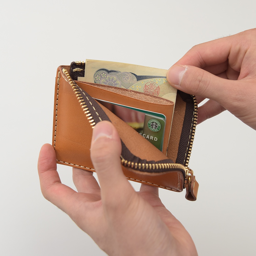 淺棕色皮革L型拉鍊迷你短夾，內有日圓紙鈔及綠色信用卡，雙手正將物品放入夾內。