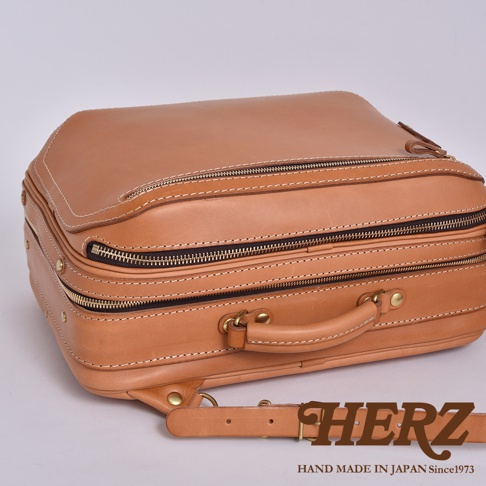 職人手作皮革兩用商務後背包，淺棕色牛皮材質，設有兩個主要拉鍊隔層，頂部有提把，可見金屬拉鍊、鉚釘與縫線細節。