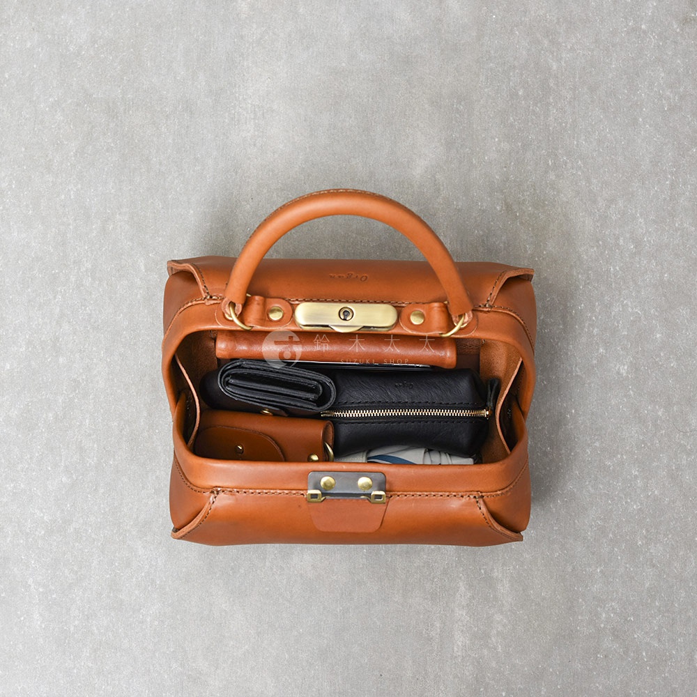 職人手作皮革Organ兩用口金手提包，採用棕色皮革製作，包身開口處有金色金屬鎖扣，內部裝有黑色皮夾和零錢包。