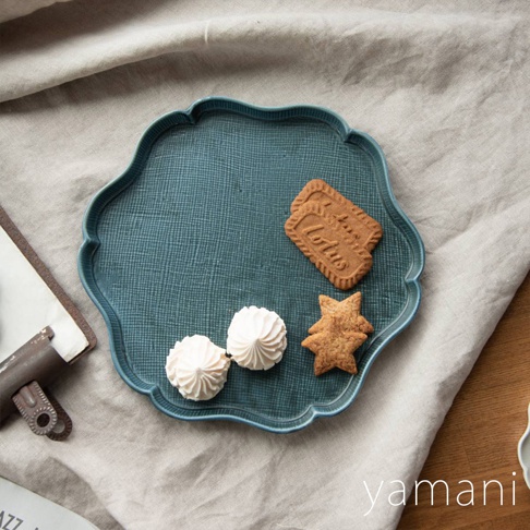 藍綠色美濃燒花型主食盤，表面有細緻的織紋，盤中擺放著兩塊 Lotus 餅乾、兩顆白色蛋白霜餅乾和兩塊星星造型餅乾。