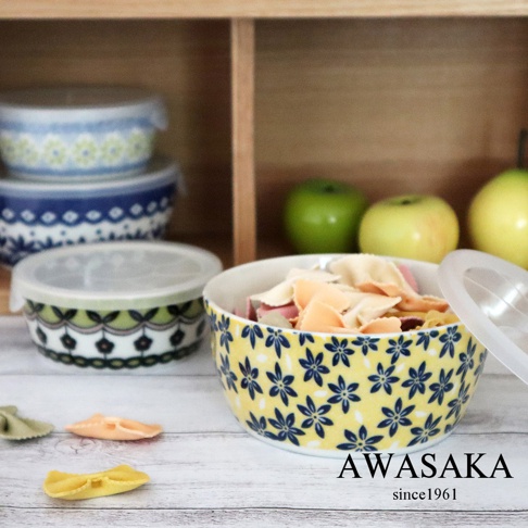 黃色陶瓷保鮮碗，飾有藍色小花圖案，碗內盛有各式義大利麵。旁邊還有數個附有透明蓋的保鮮碗，其中一個碗身有綠色和黑色的花紋。