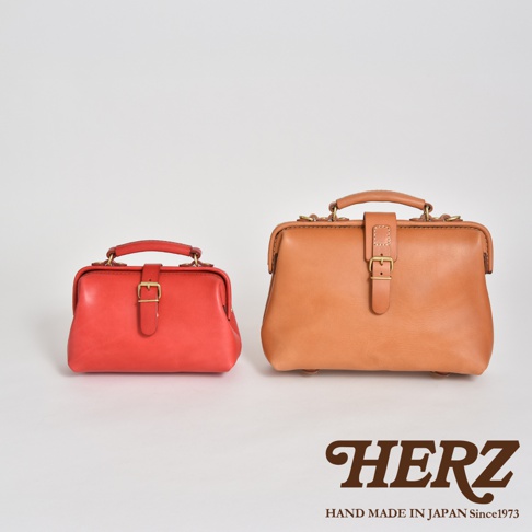 兩款職人手作皮革迷你軟皮包，左為亮紅色，右為棕褐色。兩款包均為經典醫生包款式，採用柔軟皮革製作，配有頂部提把、金屬釦環及皮帶封口設計。