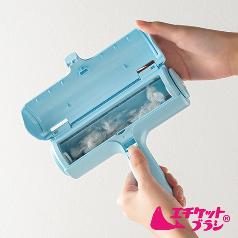 淺藍色塑膠材質的免耗材除塵滾輪，滾輪內已沾附白色棉絮，上半部蓋子打開，露出滾輪及集塵槽。