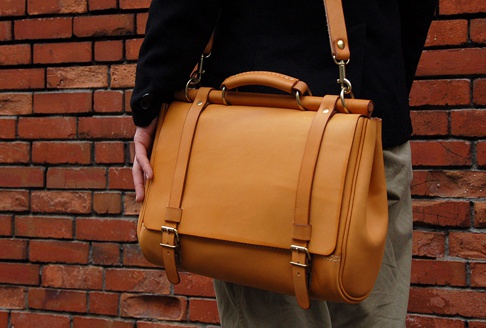 職人手作皮革屋瓦風兩用側背包，M尺寸，全粒面皮革材質，呈現溫潤的焦糖色，擁有雙皮帶搭扣與頂部提把設計，可肩背或斜背。