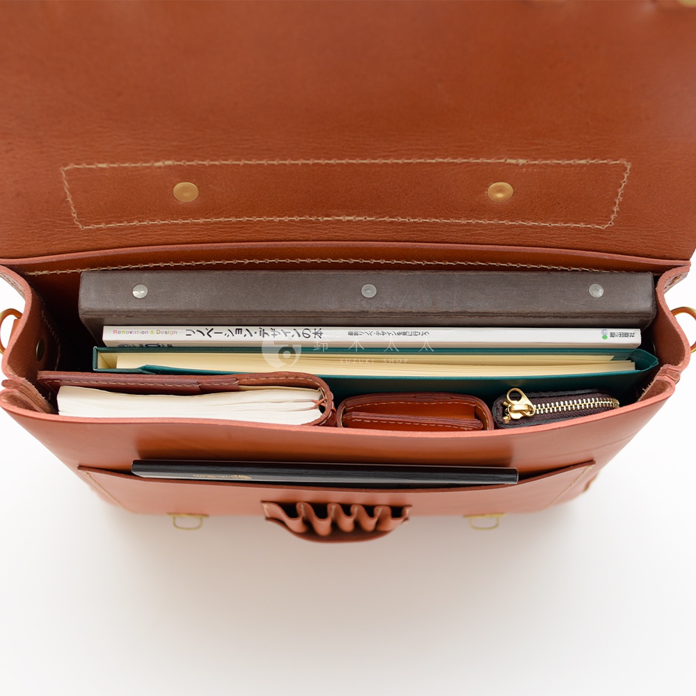 職人手作皮革傳統歐風三用學生包，內部裝有書籍、筆記本、皮夾和零錢包，整體為棕褐色。