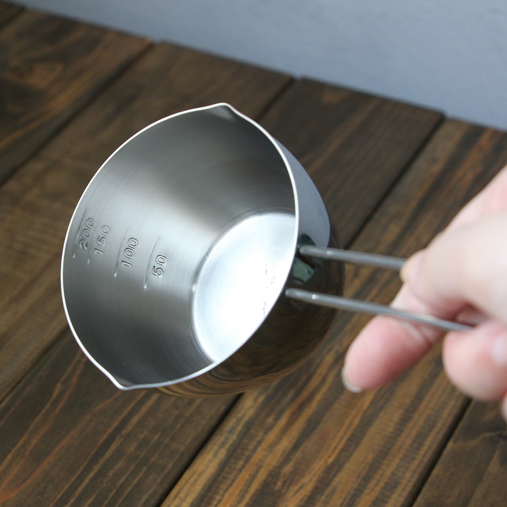 不鏽鋼長柄量杯，內部刻有50ml、100ml、150ml、200ml的刻度線，杯身呈圓筒狀，一側有傾倒口，另一側焊接著一根長長的金屬手柄，整體為銀白色金屬光澤。