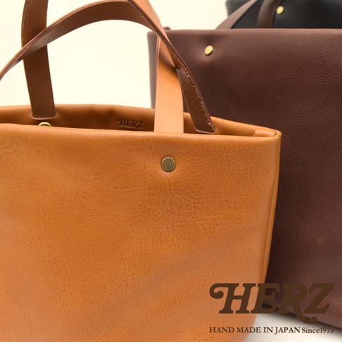 職人手作皮革托特包，前方為焦糖棕色，後方為深棕色，均為柔軟皮革材質，配有同色系皮革提把與金色金屬釦。