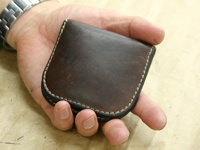 一只手拿著一個深棕色皮革製的馬蹄形零錢包，邊緣有米白色縫線。