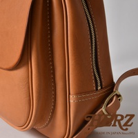 職人手作皮革迷你後背包，採用天然皮革製成，呈現溫潤的棕褐色，立體口袋設計，搭配金色拉鍊與銅色扣環，展現精緻工藝。