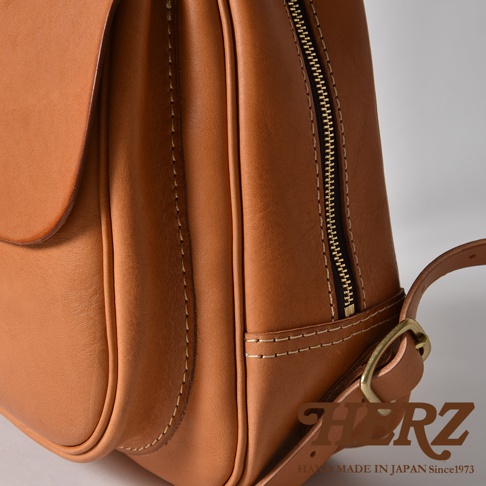職人手作皮革迷你後背包，採用天然皮革製成，呈現溫潤的棕褐色，立體口袋設計，搭配金色拉鍊與銅色扣環，展現精緻工藝。