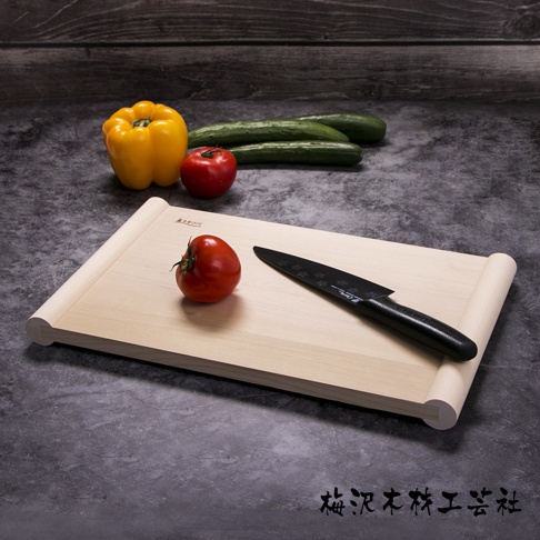 淺色木質砧板，上面放著一顆番茄和一把黑色刀具。背景有黃色甜椒和三根黃瓜。