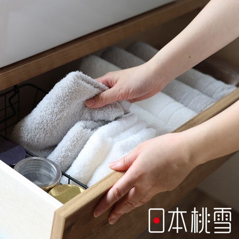 一雙手正在整理一疊淺灰色和白色的 Lite! 輕生活快適速乾薄手迷你浴巾，浴巾材質柔軟，整齊收納於木質抽屜內。