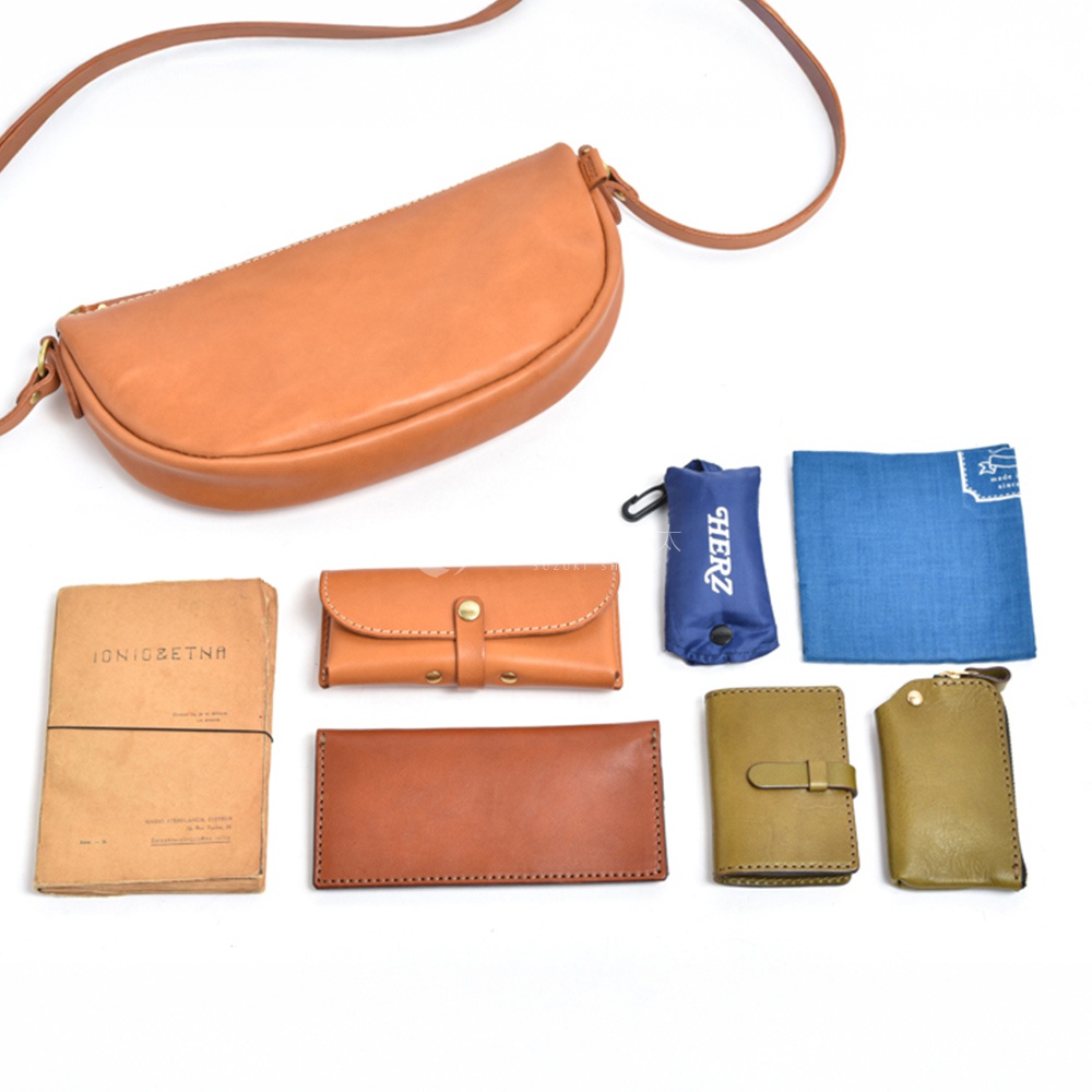 模式B： 日文書寫的紙本、皮製錢包、鑰匙包、藍色小袋和一塊藍色布料，擺放在皮革半圓馬鞍包下方。