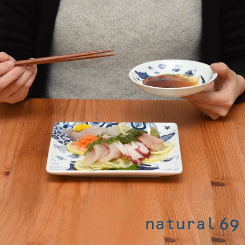 一個裝有生魚片和章魚的長方形陶瓷盤，盤上飾有藍色海洋生物圖案，旁邊有一個小圓形醬料碟，碟子裡裝有深色醬汁。