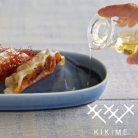 藍色長型波佐見燒主菜盤上擺放著煎餃，上面撒有細緻的紅絲，一隻手正從透明玻璃瓶中淋下淺黃色液體。