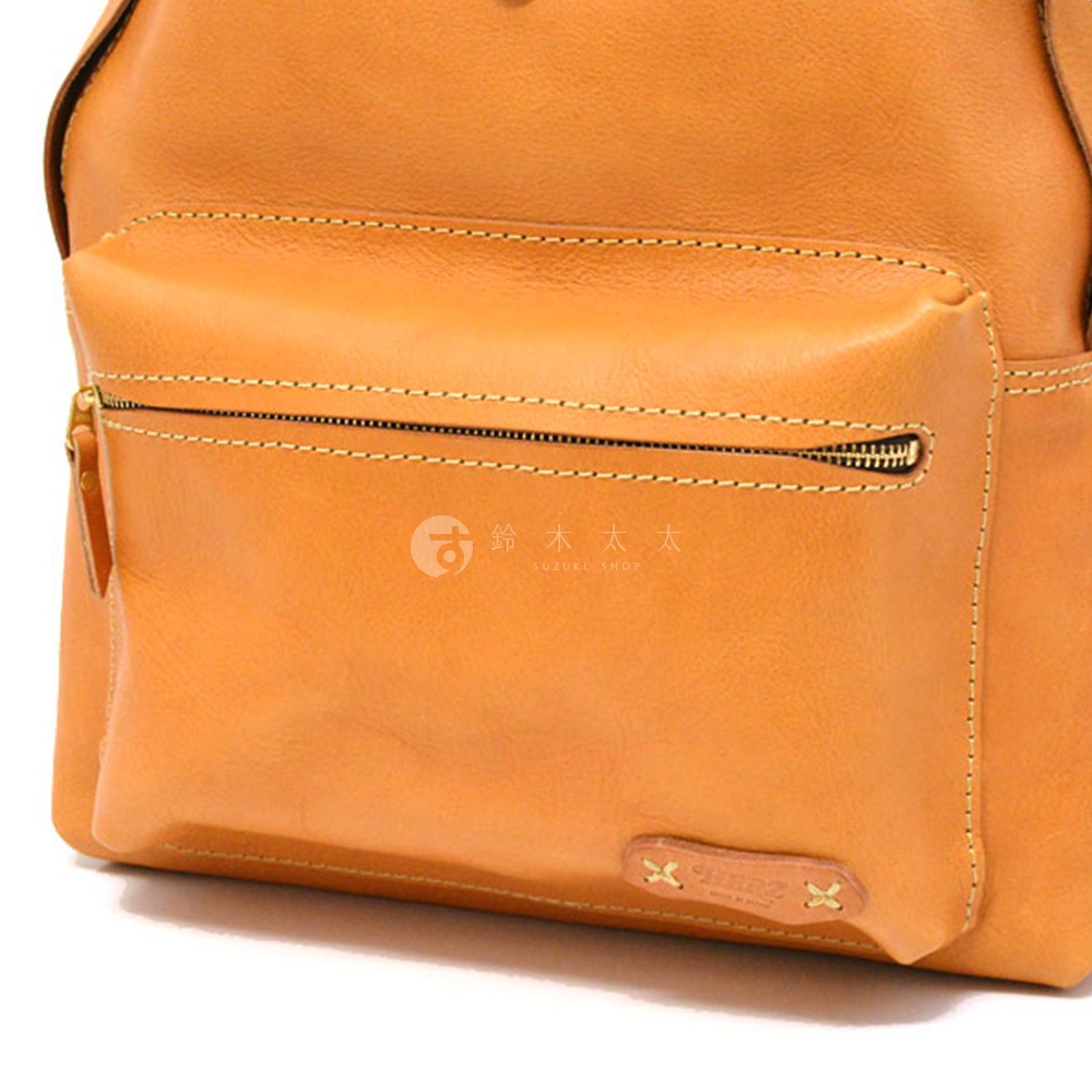 淺棕色皮革後背包，正面有一個拉鍊口袋，有明顯的縫線細節，底部有品牌標誌。