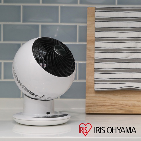 白色IRIS OHYAMA PCF-SC15T 空氣循環扇，帶有黑色扇葉和網罩，擺放在白色檯面上，背景為淺藍色磚牆和木質砧板。