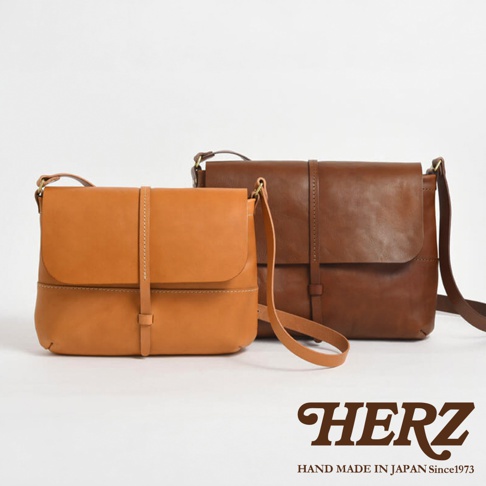 模式B： 兩只手工製作的HERZ皮革馬鞍包，分別為棕褐色和深棕色，以純淨的白色背景呈現。