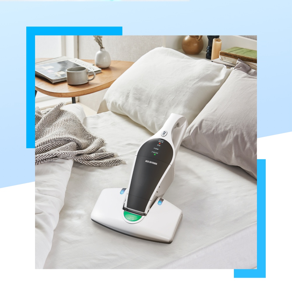 IRIS OHYAMA 充電式塵蟎機 IC-FDC-1T 放在鋪著白色床單的床上，床頭有枕頭、一本書和一個杯子