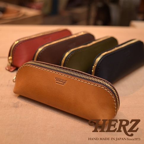 五款職人手作皮革三角收納筆袋，包含焦糖棕、酒紅、深棕、軍綠、海軍藍，皆以真皮製作，搭配金色拉鍊。