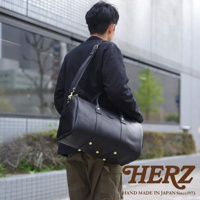 一個男人身背黑色皮革波士頓包，包上有金色鉚釘和可調節肩帶。