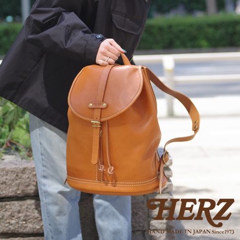 職人手作皮革單扣束口後背包，採用棕色皮革製成，配有可調節肩帶和束口設計，整體風格簡約實用。
