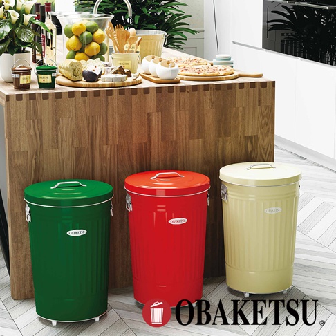 由左至右分別是綠色、紅色和黃色的 OBAKETSU 手工製附輪垃圾桶，垃圾桶上方擺放著餐盤、水果和麵包，背景是廚房島台與櫥櫃。