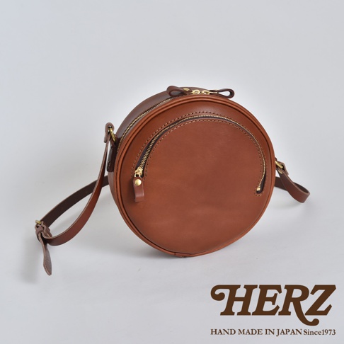 職人手作皮革小圓包，採用圓潤的設計，主體為棕色皮革，配有金色拉鍊。包身設有兩個拉鍊口袋，肩帶可調節。