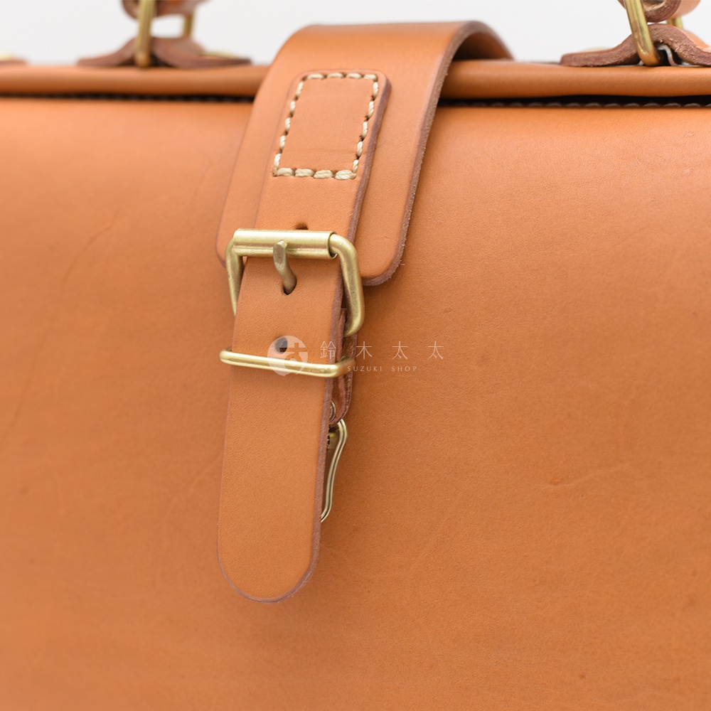 職人手作皮革軟式杜勒斯包，特寫其黃褐色皮革材質，搭配金色金屬釦環和皮質錶帶，展現細膩工藝。