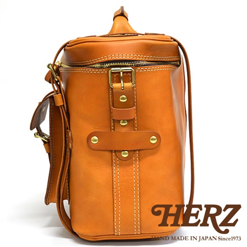 職人手作皮革大型三用旅行後背包，呈現自然棕色皮革，帶有黃銅色金屬扣環和拉鍊，以及清晰的白色縫線。包身設計簡潔，側面有可調節的皮帶和扣子。