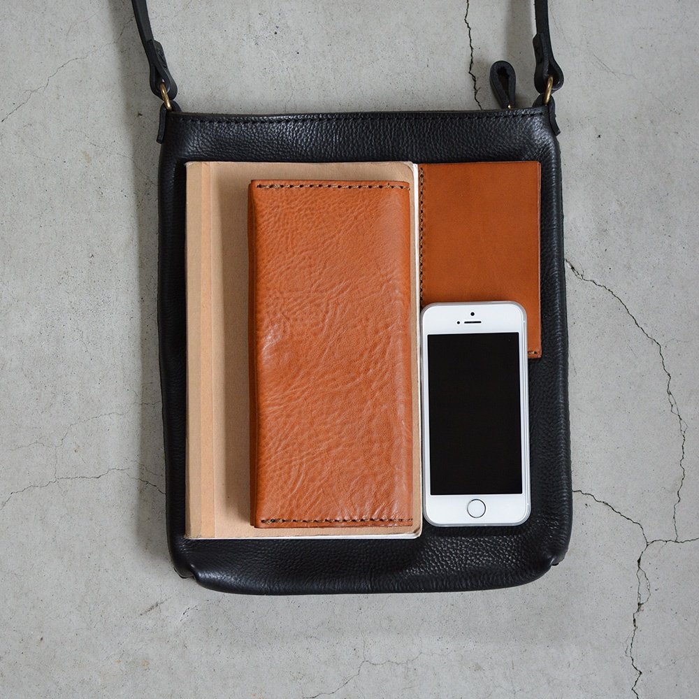 黑色皮革肩背包內有兩本筆記本、一個棕色皮革長夾和一支白色手機。