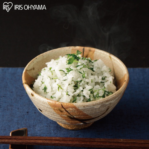 一碗盛滿熱氣騰騰的越光米飯，米粒飽滿，點綴著翠綠的香草，裝在一個帶有大地色紋理的陶碗中，碗旁放著一雙筷子，背景為深色。