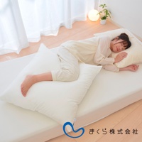 一名女子側臥在白色床墊上，腿部夾著一個白色長方形枕頭，頭部倚靠著另一個較小的奶油色枕頭。