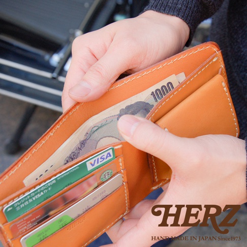 皮革雙折短夾，以淺棕色皮革製成，內有日圓鈔票與信用卡，包括一張 VISA 卡。