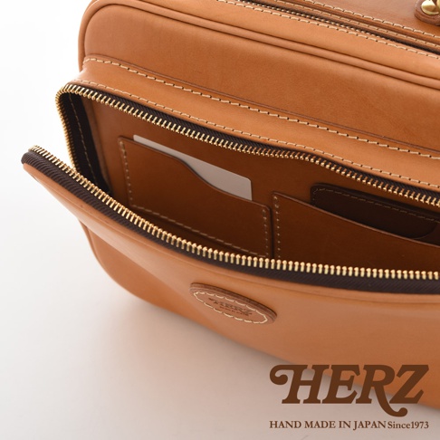 駝色皮革製成的兩用商務公事包，拉鍊部分打開，露出內部有卡槽及隔層。包身上有壓印品牌標誌。