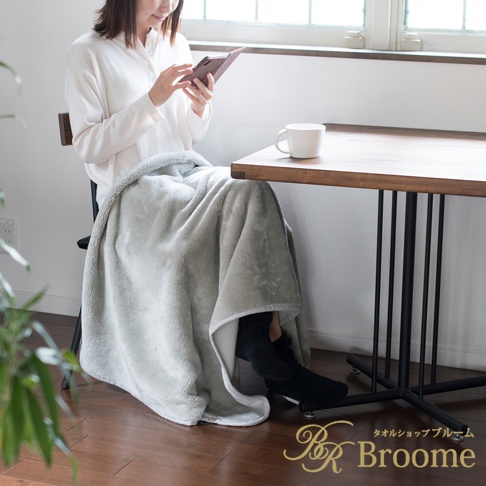 淺灰色毛絨保暖毯，質地柔軟，覆蓋在一位女士的腿上，她坐著使用平板電腦。毯子邊緣有白色滾邊。