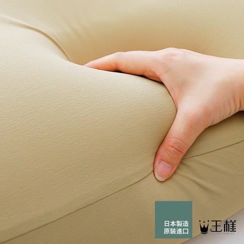 模式B： 一張手正按壓著米駝色枕頭的特寫照片，枕頭材質呈現細膩紋理，具有良好的支撐性，右下角有日文「日本製造 原裝進口」及「王樣」品牌標誌。