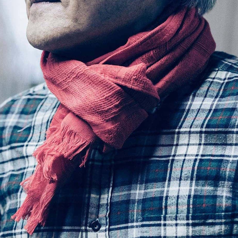 粉紅色今治匹馬棉圍巾，帶有流蘇邊飾，圍繞在穿著格紋襯衫的人的脖子上。
