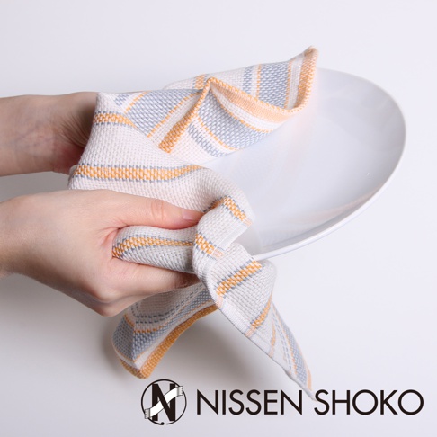 一條今治純棉廚房擦拭巾，帶有橘色、灰色和白色條紋，由雙手拿取，放在白色盤子上。