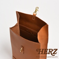 職人手作皮革紙袋風後背包，採用光滑棕色皮革材質，包身結構立體，內有隔層設計，頂部有金色鉤扣和皮革提把。