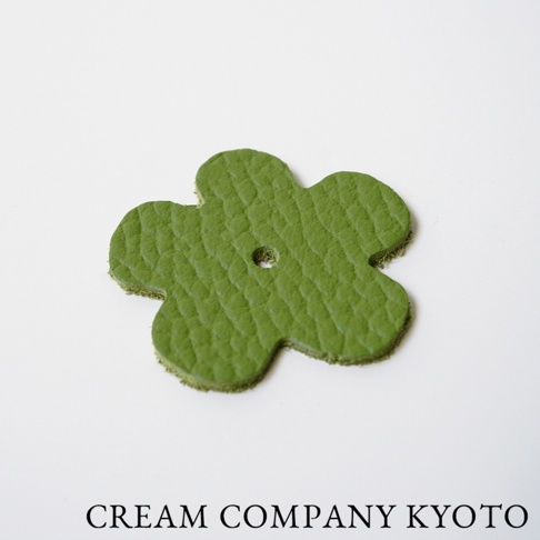 綠色皮革製成的五瓣花形吊飾，表面有紋理，中央有一個小孔。