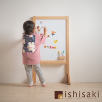 木製框架的兒童多功能繪畫白板，白板上貼有彩色磁性數字和動物造型，並用綠色筆書寫。一名穿著粉色印花T恤和豹紋長褲的小孩正在白板上作畫。