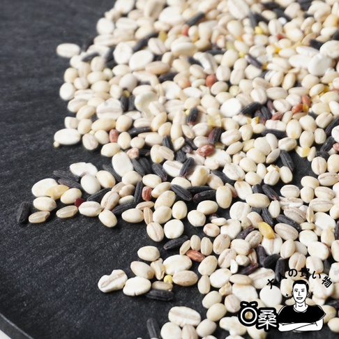一堆混合的穀物，包含多種米類和豆類，顏色有白色、淺褐色、黑色和少量紅色，質地顆粒分明。